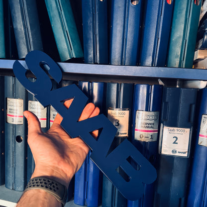 Hand holding a blue 'Saab' sign in front of blue boxes with Saab labels.